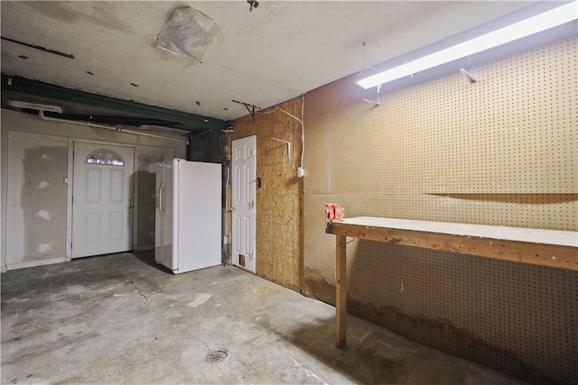 unfinished basement featuring freestanding refrigerator and a workshop area