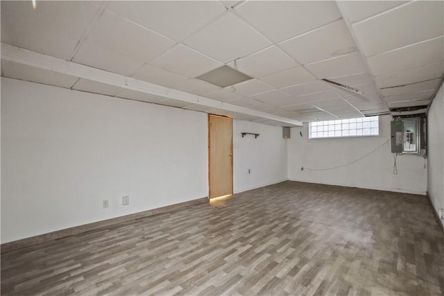 basement featuring a paneled ceiling, electric panel, and wood finished floors