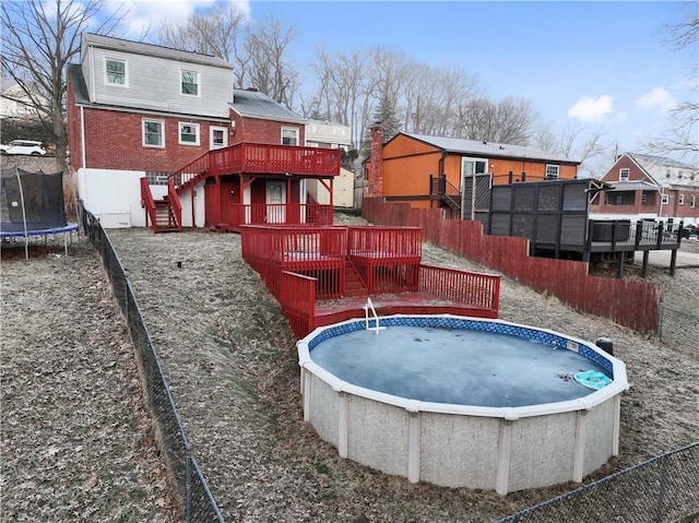 pool with a deck, stairway, a trampoline, and a fenced backyard