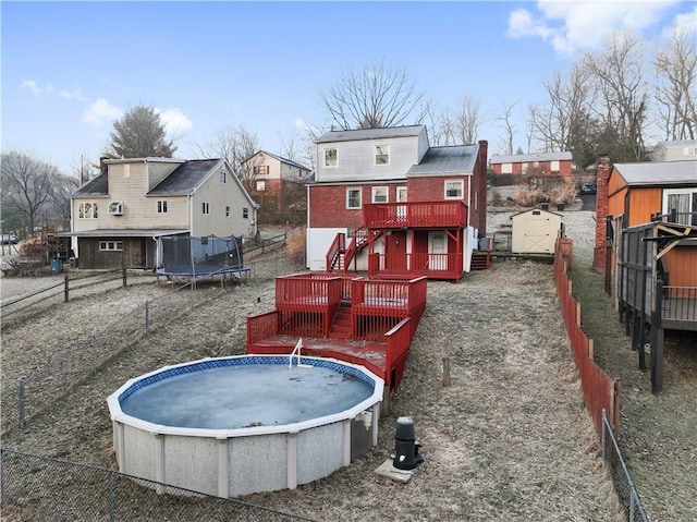 rear view of house featuring a trampoline, an outbuilding, a shed, a wooden deck, and stairs