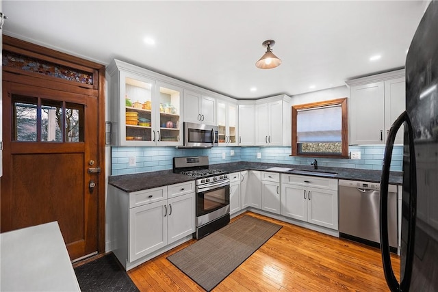 kitchen with stainless steel appliances, a sink, light wood-style floors, decorative backsplash, and dark countertops