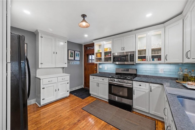 kitchen with appliances with stainless steel finishes, white cabinets, light wood-style flooring, and decorative backsplash