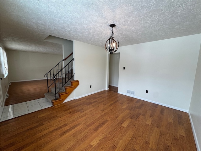 interior space featuring a notable chandelier, wood finished floors, visible vents, baseboards, and stairway