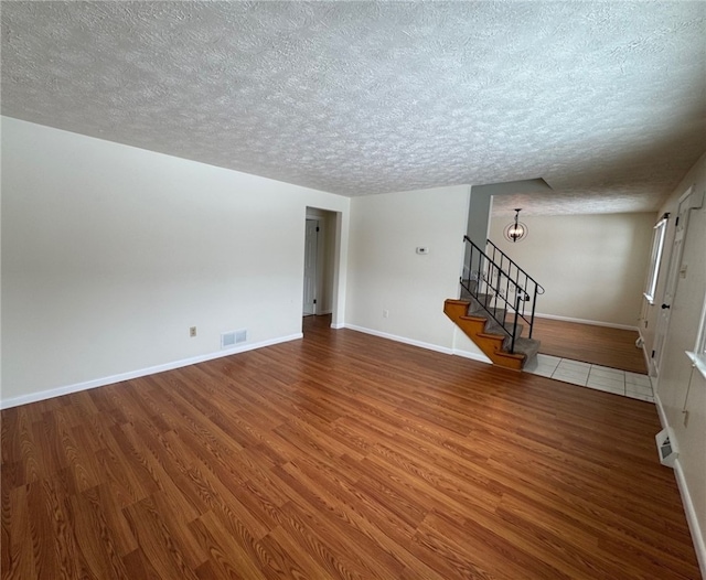 unfurnished room with stairway, wood finished floors, visible vents, and baseboards