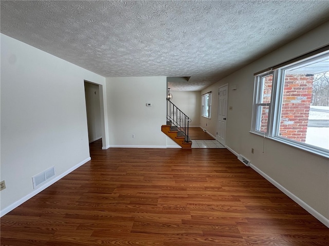 unfurnished living room with plenty of natural light, visible vents, stairway, and wood finished floors