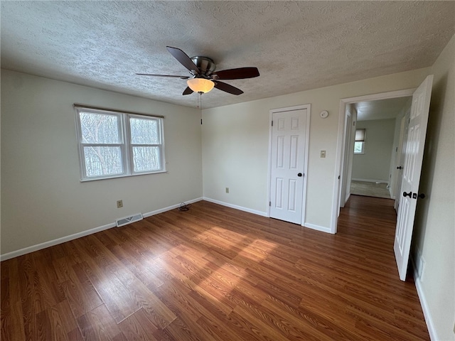 unfurnished bedroom featuring visible vents, a ceiling fan, a textured ceiling, wood finished floors, and baseboards