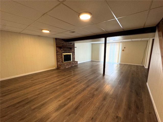 finished basement featuring a brick fireplace, wood finished floors, a paneled ceiling, and baseboards