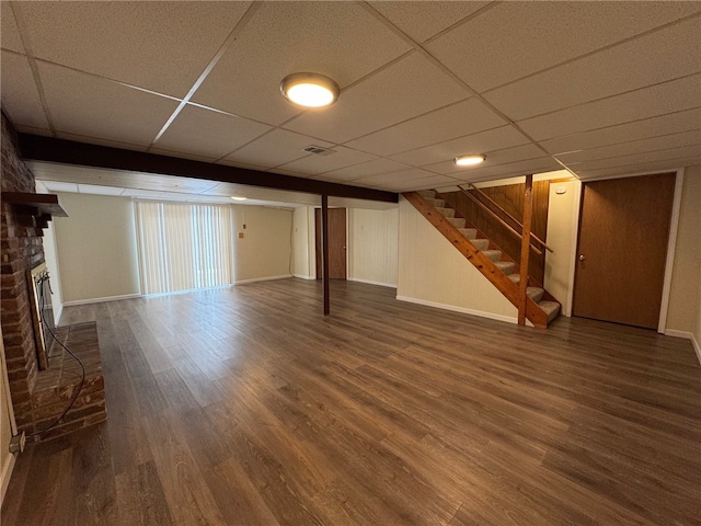 finished basement with a paneled ceiling, a brick fireplace, stairway, and wood finished floors