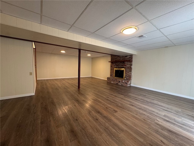 finished below grade area with a fireplace, visible vents, wood finished floors, a drop ceiling, and baseboards