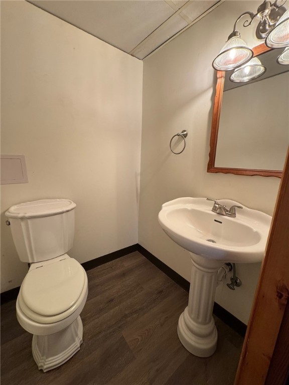 half bath with toilet, baseboards, and wood finished floors