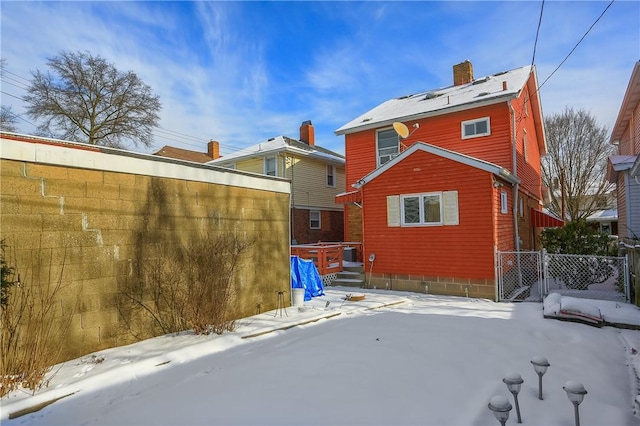 snow covered rear of property featuring a chimney and fence