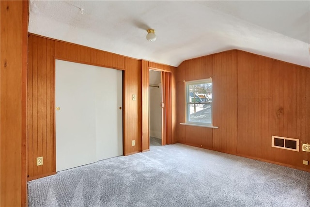 unfurnished bedroom with visible vents, multiple closets, carpet, wood walls, and lofted ceiling