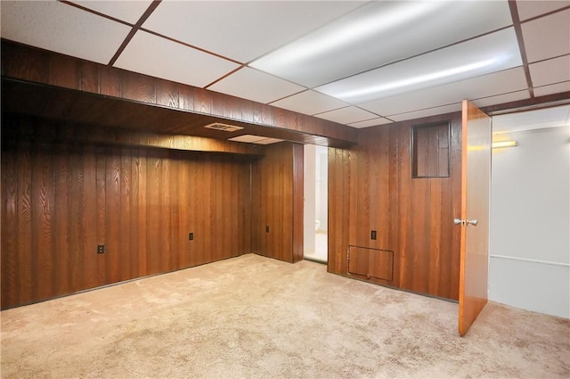 finished basement with a drop ceiling, wood walls, and carpet floors