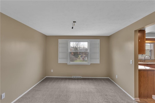 unfurnished room with light carpet, baseboards, visible vents, and a sink