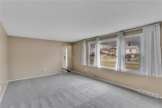 empty room featuring a textured ceiling, carpet flooring, visible vents, and baseboards