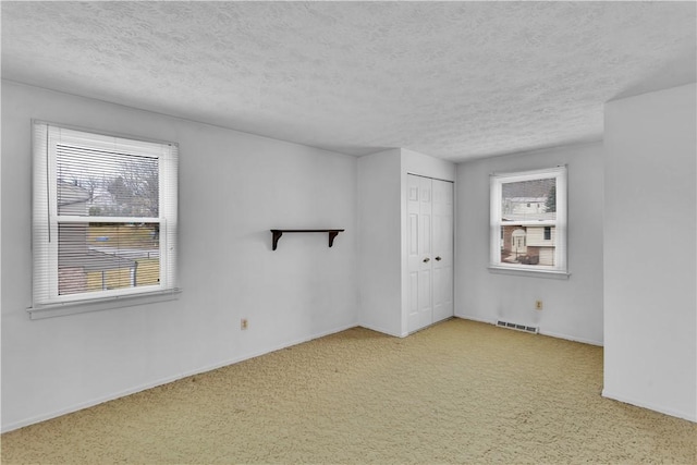 unfurnished room with carpet floors, visible vents, a textured ceiling, and baseboards