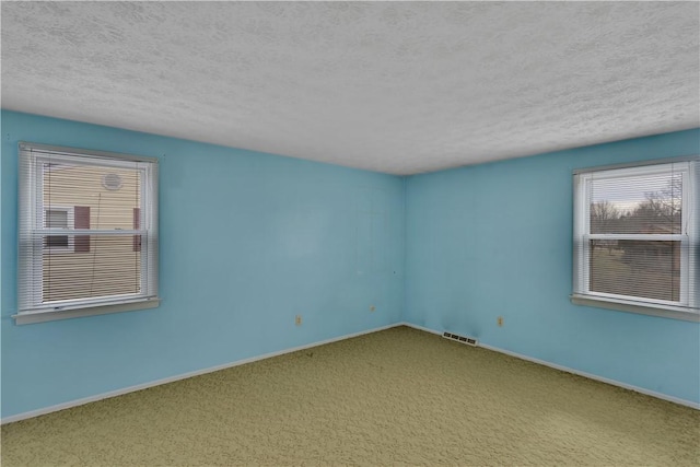 carpeted spare room with baseboards, visible vents, and a textured ceiling