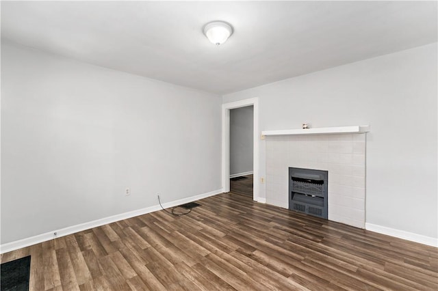 unfurnished living room with a tiled fireplace, baseboards, and wood finished floors