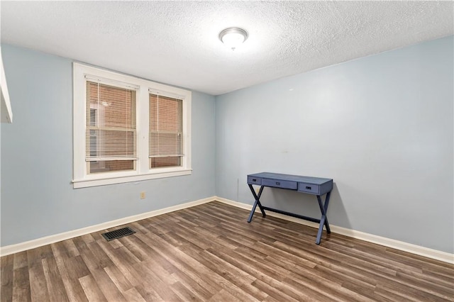 empty room with visible vents, a textured ceiling, baseboards, and wood finished floors