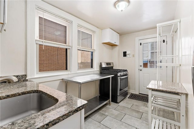 kitchen with light tile patterned flooring, a sink, white cabinetry, light stone countertops, and stainless steel range with gas stovetop