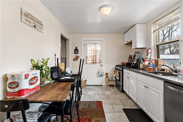 kitchen featuring light tile patterned floors, dark stone counters, stainless steel appliances, white cabinetry, and a sink