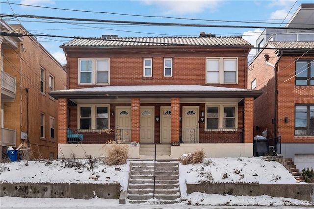 view of front facade featuring a tile roof, a porch, and brick siding