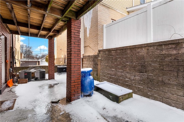 snow covered patio featuring central air condition unit and fence