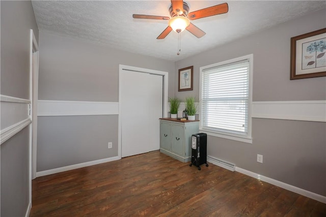 spare room with baseboards, a ceiling fan, wood finished floors, a textured ceiling, and a baseboard heating unit