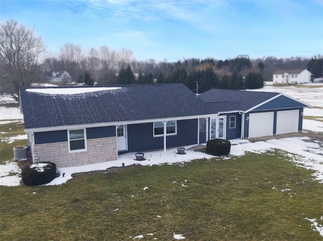 ranch-style home with a front yard, stone siding, roof with shingles, an attached garage, and central AC