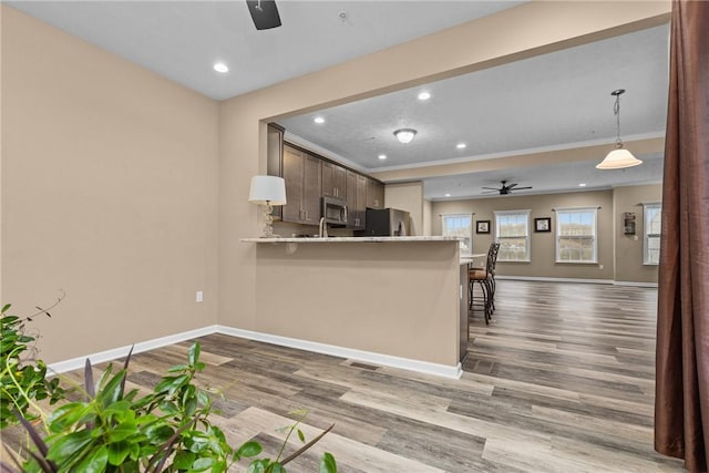 kitchen with baseboards, a ceiling fan, wood finished floors, a peninsula, and stainless steel appliances