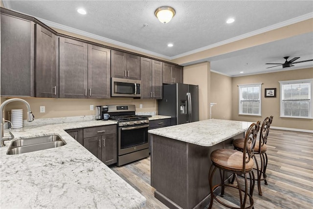 kitchen with a breakfast bar area, a center island, stainless steel appliances, dark brown cabinets, and a sink