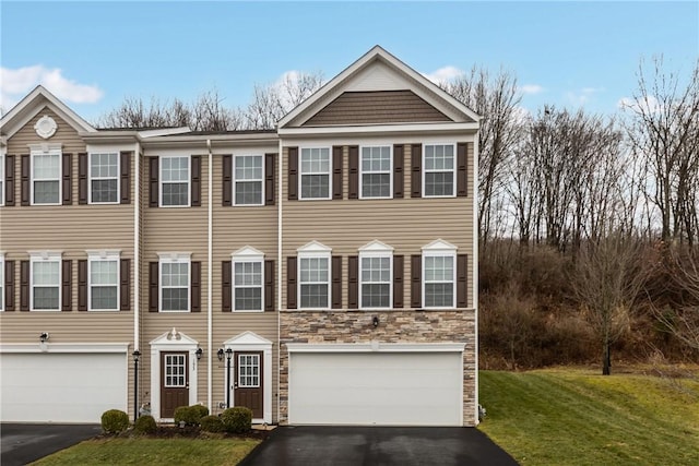 view of property featuring aphalt driveway, a front yard, stone siding, and an attached garage