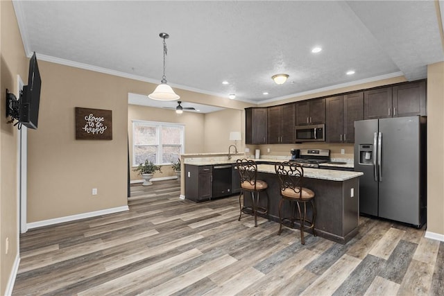 kitchen featuring dark brown cabinetry, appliances with stainless steel finishes, a center island, light wood finished floors, and crown molding