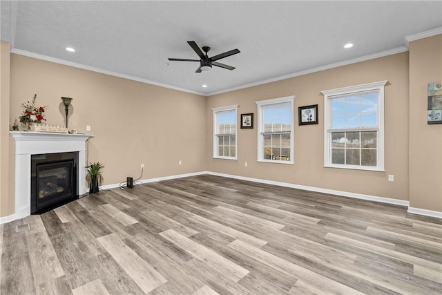 unfurnished living room featuring ornamental molding, a glass covered fireplace, baseboards, and wood finished floors