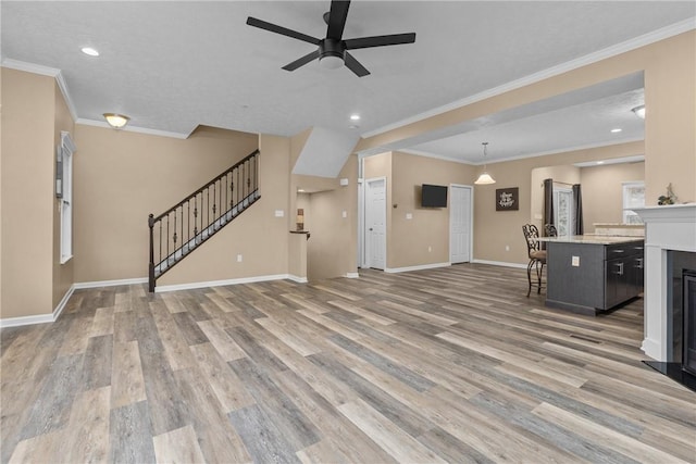 unfurnished living room featuring ceiling fan, baseboards, light wood-style floors, stairway, and crown molding