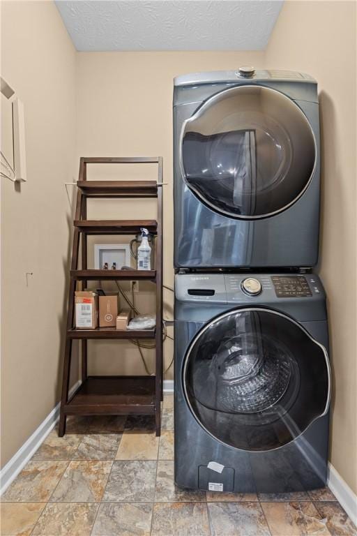 clothes washing area featuring stacked washer and clothes dryer, stone finish floor, a textured ceiling, and baseboards