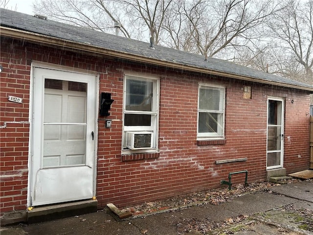 doorway to property featuring brick siding, a shingled roof, and cooling unit