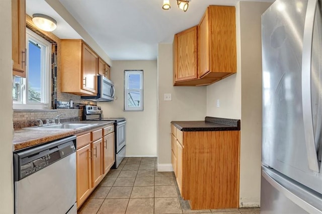 kitchen with baseboards, decorative backsplash, appliances with stainless steel finishes, a sink, and light tile patterned flooring