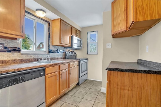 kitchen featuring light tile patterned floors, stainless steel appliances, tasteful backsplash, a sink, and baseboards