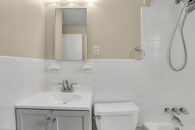 full bath with a wainscoted wall, tile walls, bathing tub / shower combination, toilet, and vanity