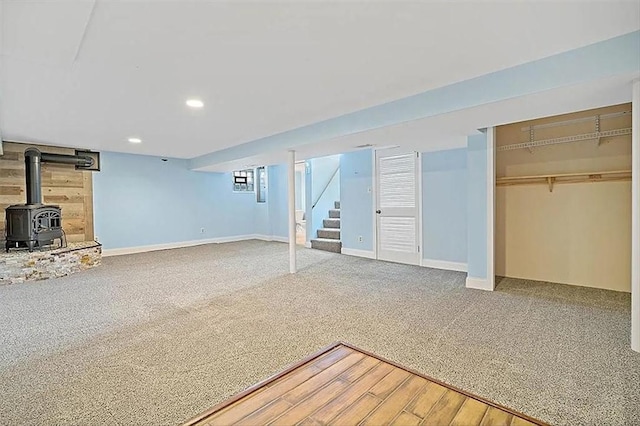 finished below grade area featuring recessed lighting, light colored carpet, stairway, a wood stove, and baseboards