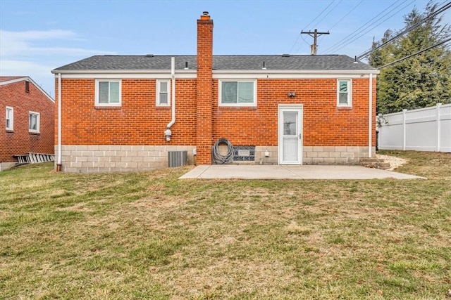 rear view of house featuring a patio, brick siding, fence, a yard, and a chimney