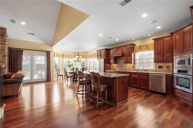 kitchen featuring dark wood-style floors, custom exhaust hood, stainless steel appliances, visible vents, and a kitchen bar