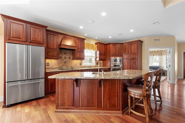 kitchen with stainless steel appliances, premium range hood, visible vents, and light wood-style floors