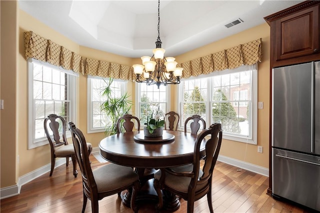 dining space featuring visible vents, a raised ceiling, baseboards, light wood-style flooring, and a chandelier