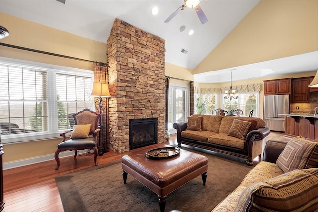 living room featuring a fireplace, high vaulted ceiling, light wood-type flooring, baseboards, and ceiling fan with notable chandelier