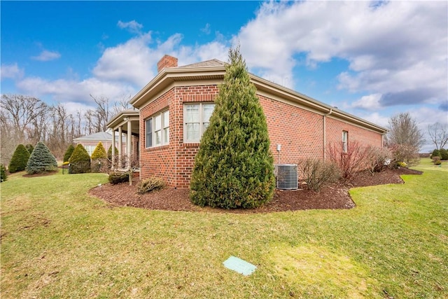 view of home's exterior with brick siding, a chimney, a lawn, and central air condition unit