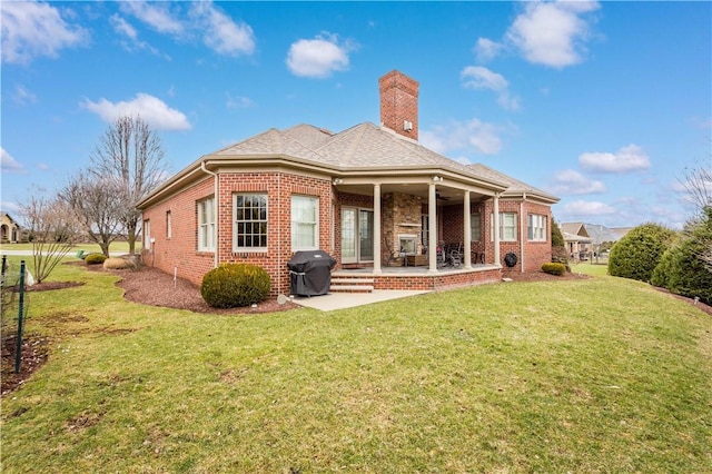 rear view of property featuring a yard, brick siding, a patio, and a chimney