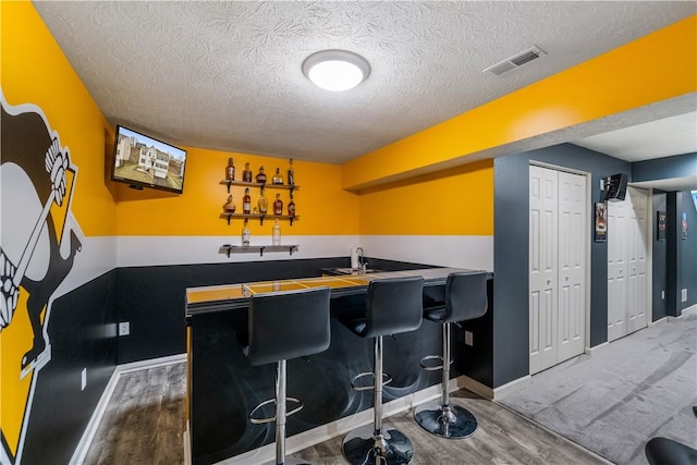 bar with visible vents, a textured ceiling, wood finished floors, wet bar, and baseboards