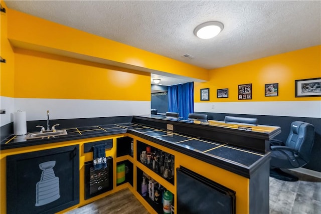 kitchen with dark countertops, a textured ceiling, a sink, and wood finished floors